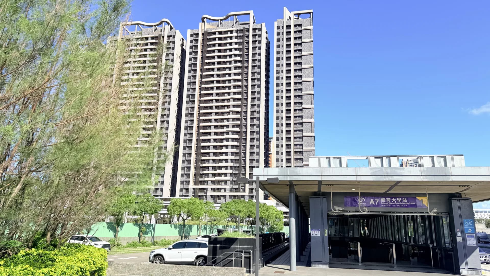 藍天下的機場捷運 A7 體育大學站入口、綠化與後方住宅大樓
